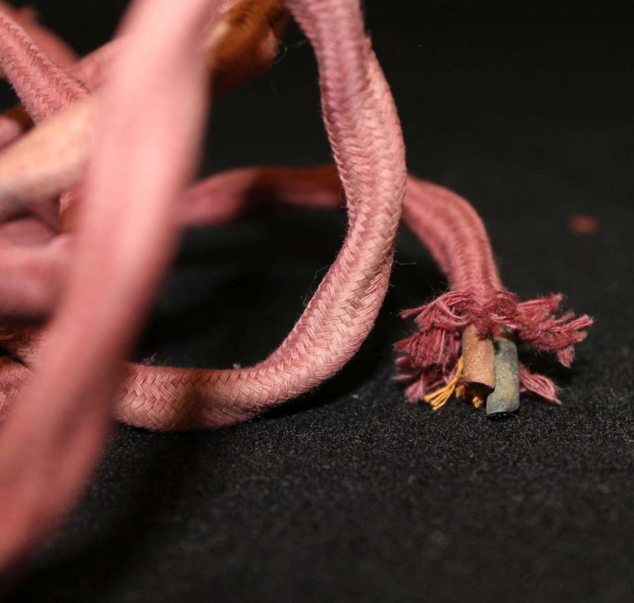 Pink braided cords with a frayed, multicolored end on a black surface