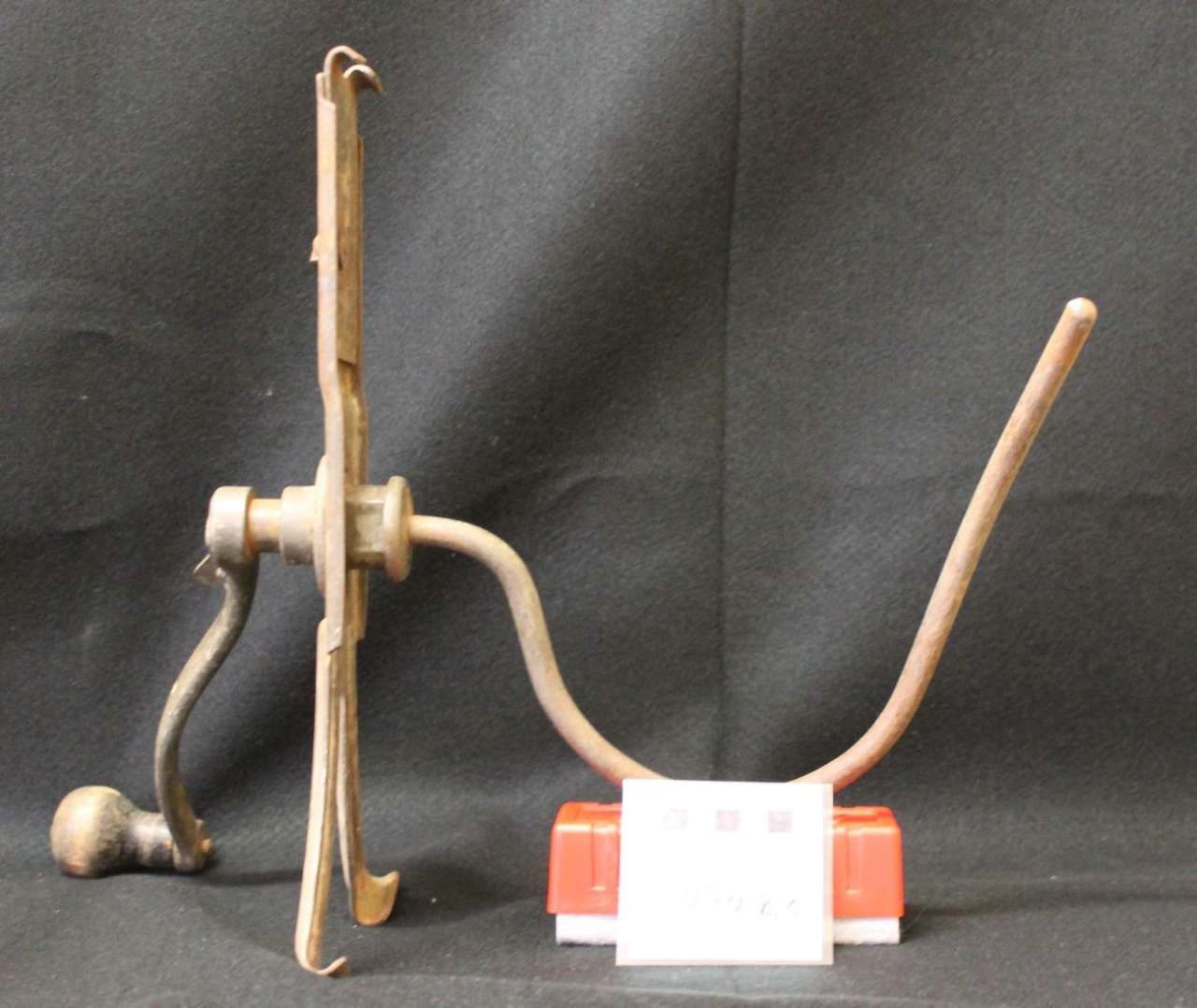 Small mechanical device with a red base, white center, and two curved wire arms on a dark background