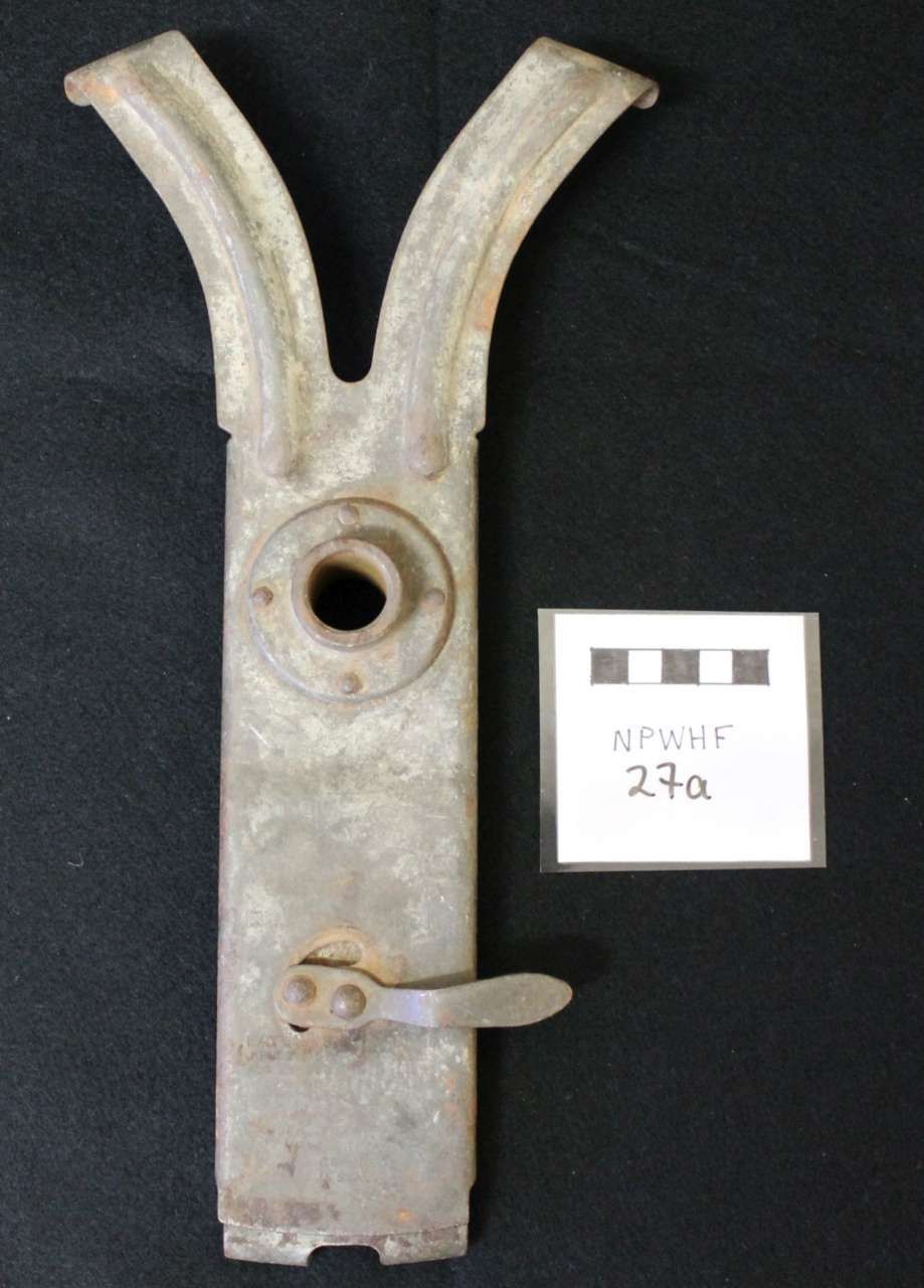 Metal Y-shaped latch or mechanism with a circular opening, shown on a black background with a small label.