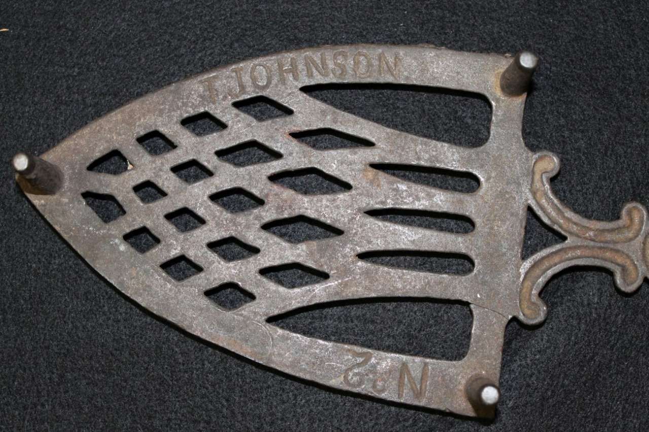 Antique metal fireplace trivet with cutout pattern on a black background