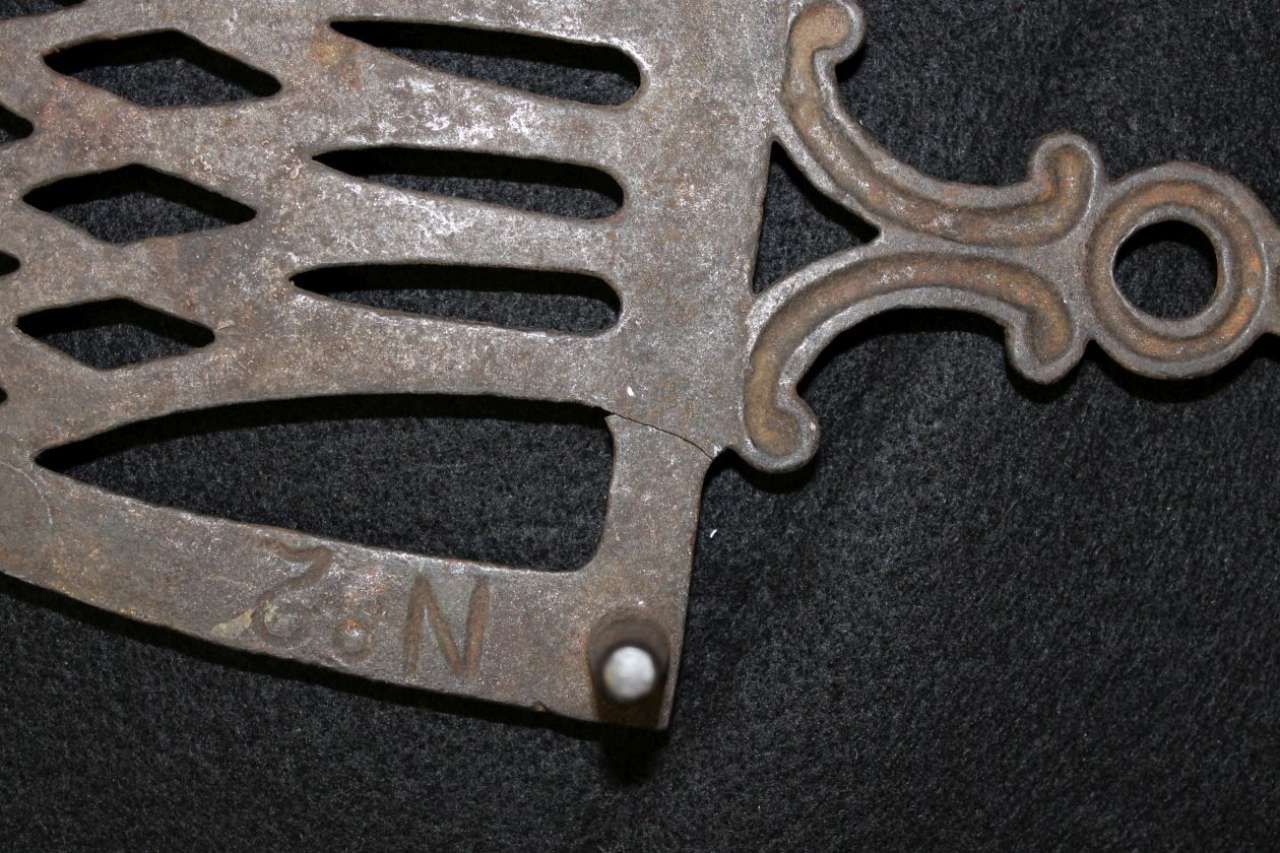 Close-up of a black metal decorative grille with a small rivet and curved brown scrollwork on dark fabric.