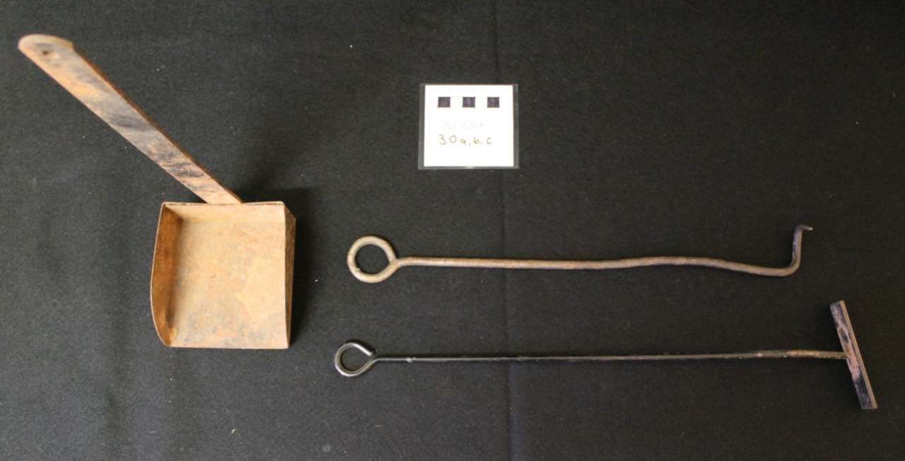 Wooden box, small sign, and two long metal rods with ring handles on a black background