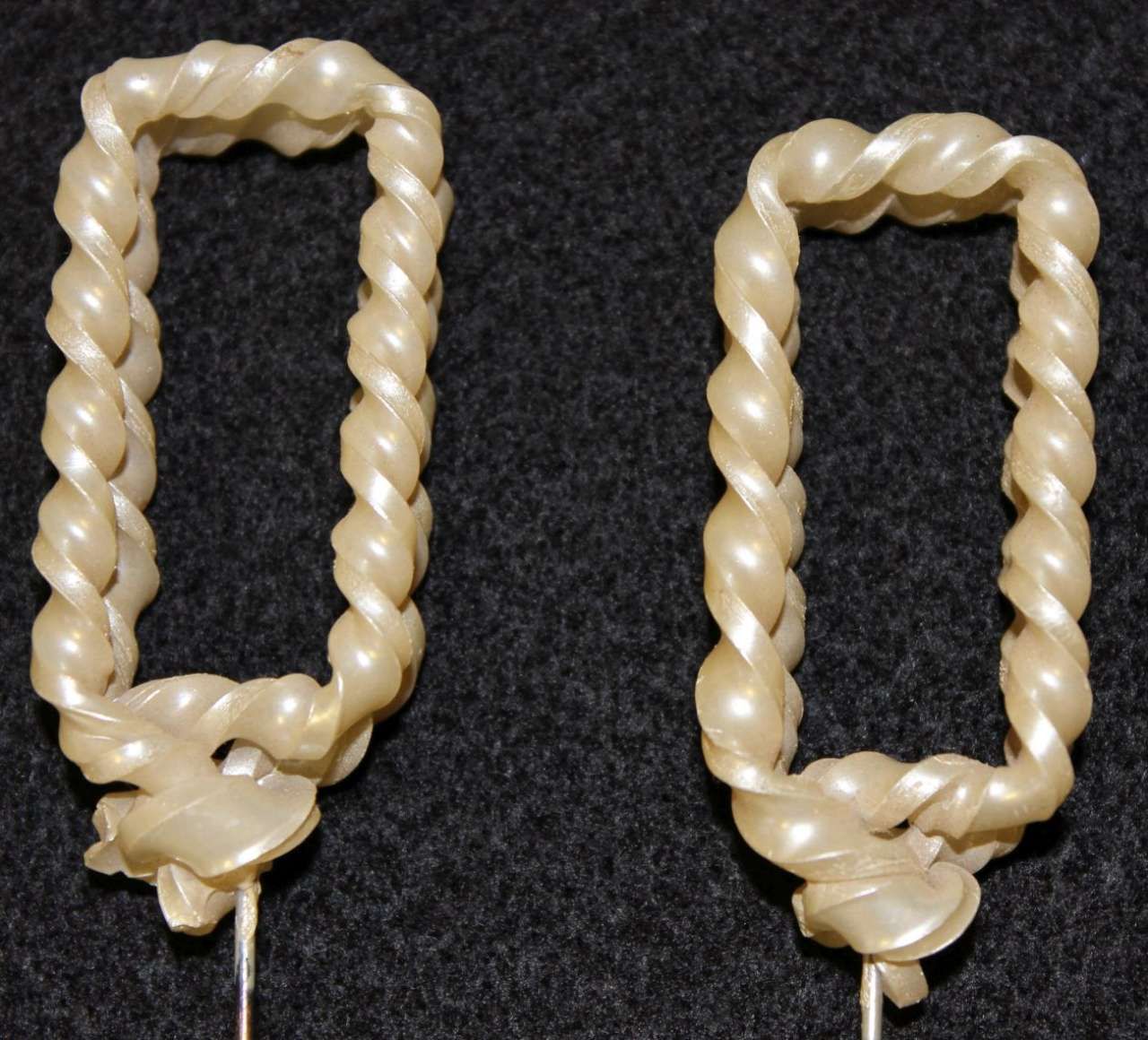 Two beige twisted candles shaped like looped rectangles on a dark background