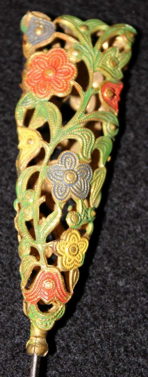 Ornate floral metal ornament with green, orange, and gold filigree on black background