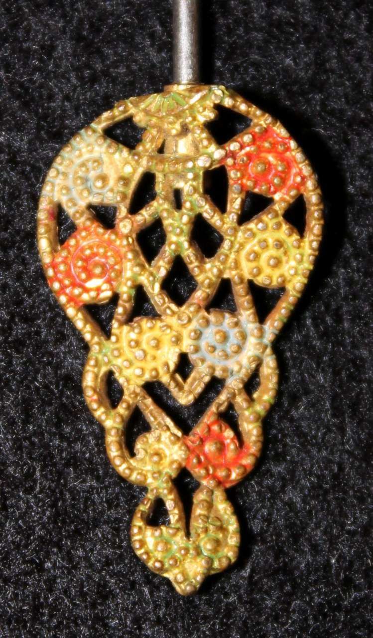 Ornate gold pendant with red, white, and black jeweled accents on a dark background