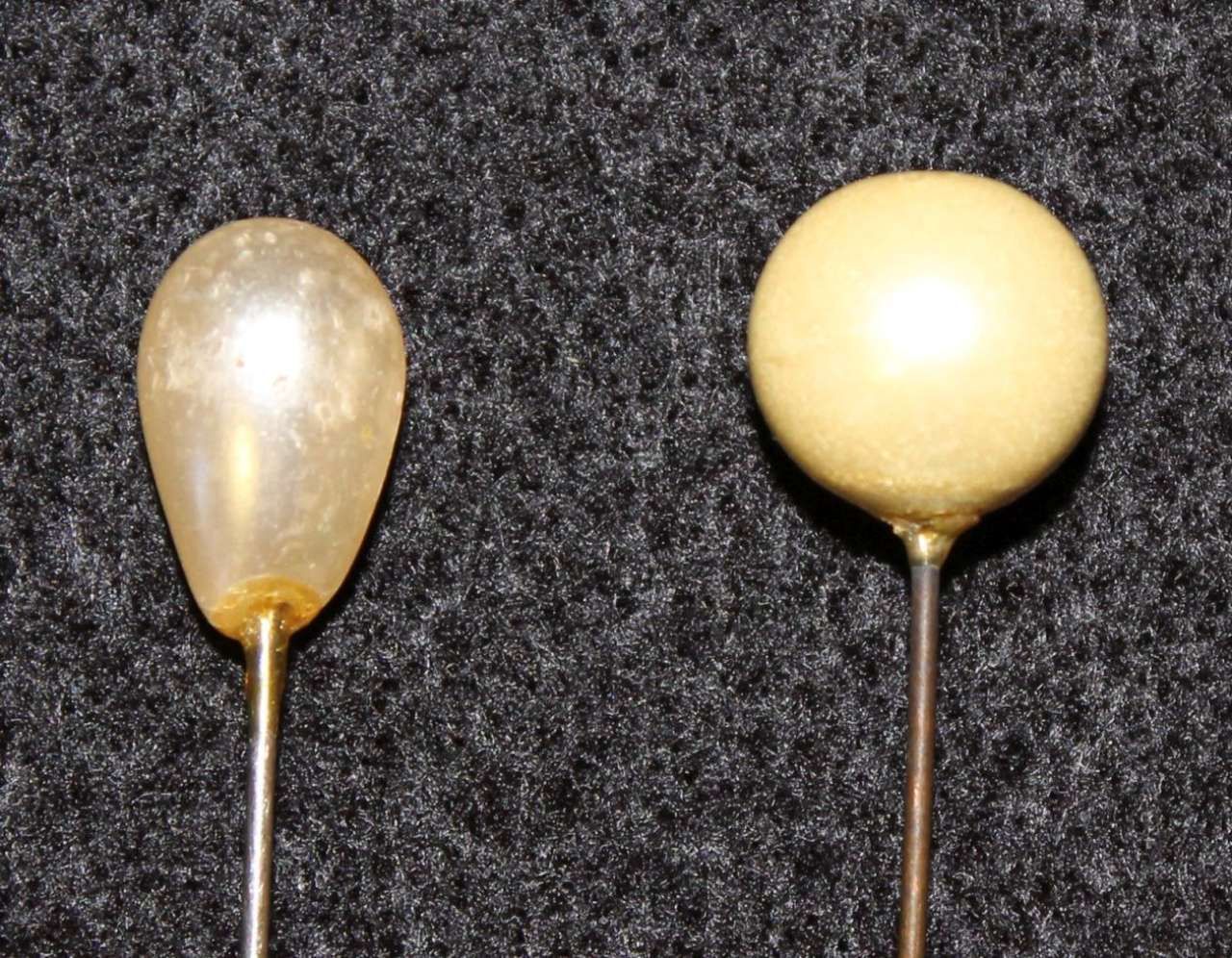 Two small balloon-shaped objects on thin wires, one translucent amber and one pale yellow, on a dark background