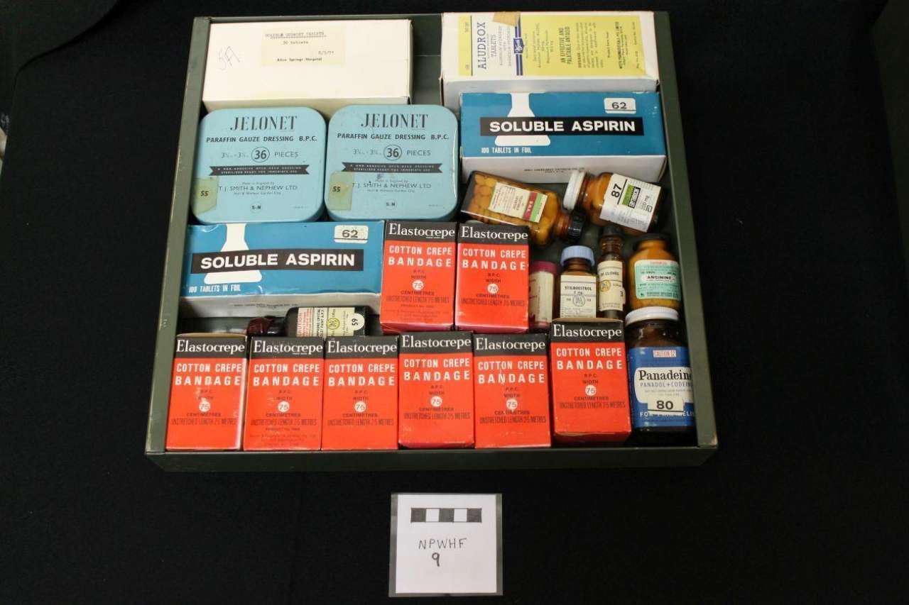 Assorted medicine bottles and boxes arranged in a display case on a black background.