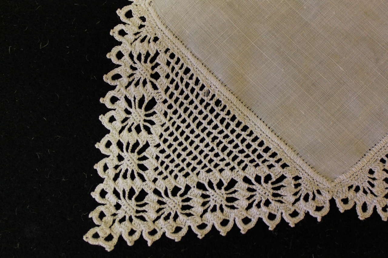 Close-up of a beige lace-trimmed handkerchief on a dark background