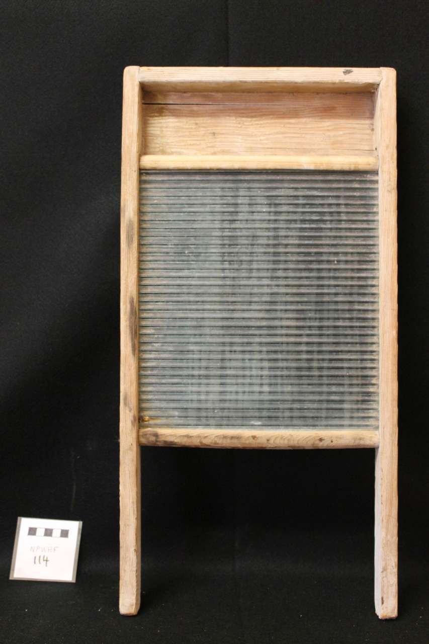 Wooden washboard with a metal scrubbing surface, shown against a dark background.