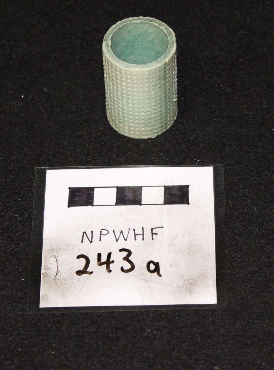 Small green cylindrical container above a label reading “NPWHF 243a” with a black-and-white scale.