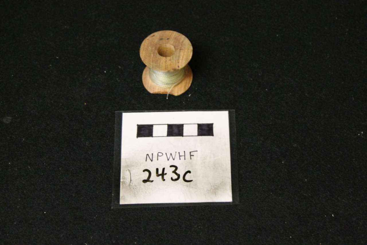 Small wooden spool above a labeled card on a black background.