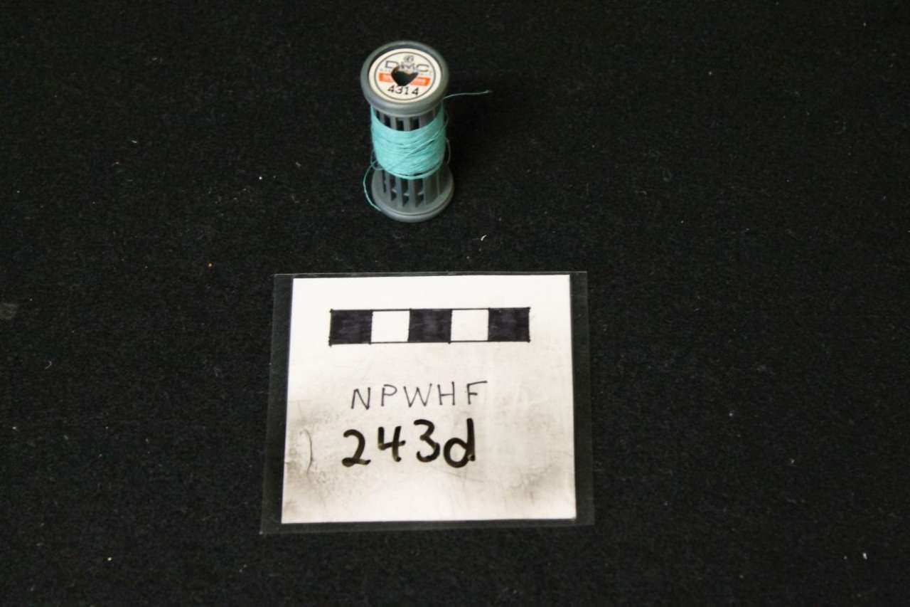 Small turquoise cylindrical container above a white label card marked “243d” on a black background.