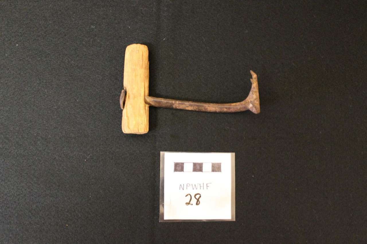 Old rusty hammer with wooden handle on a black background next to a small label.