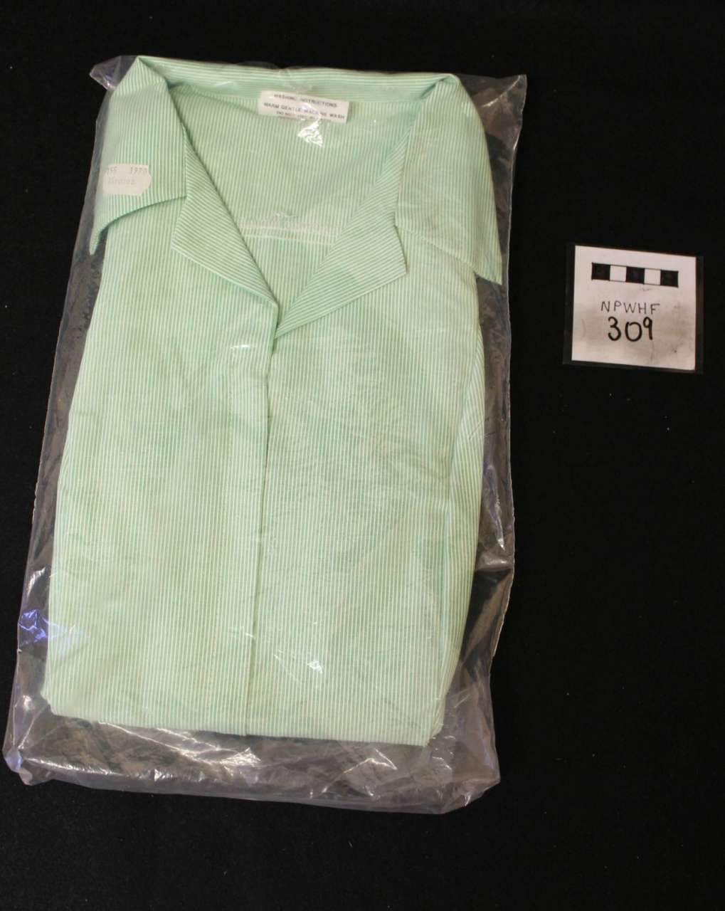 Folded mint green striped shirt in plastic packaging beside a small price card on a black background.