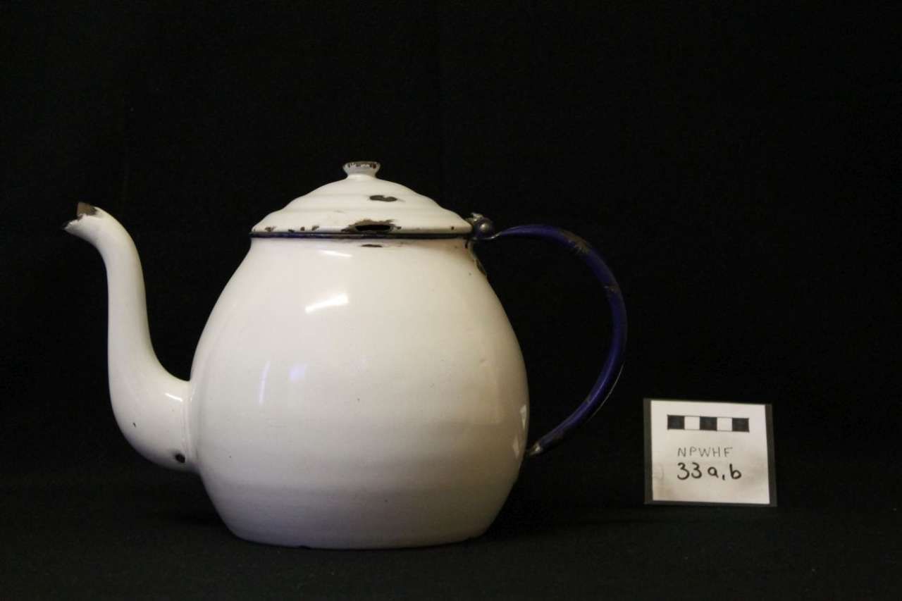 White teapot with blue handle on black background, displayed beside a small label.