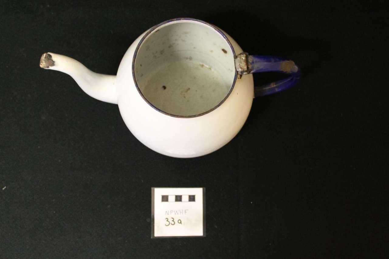 White teapot with blue handle and spout on a black background, viewed from above