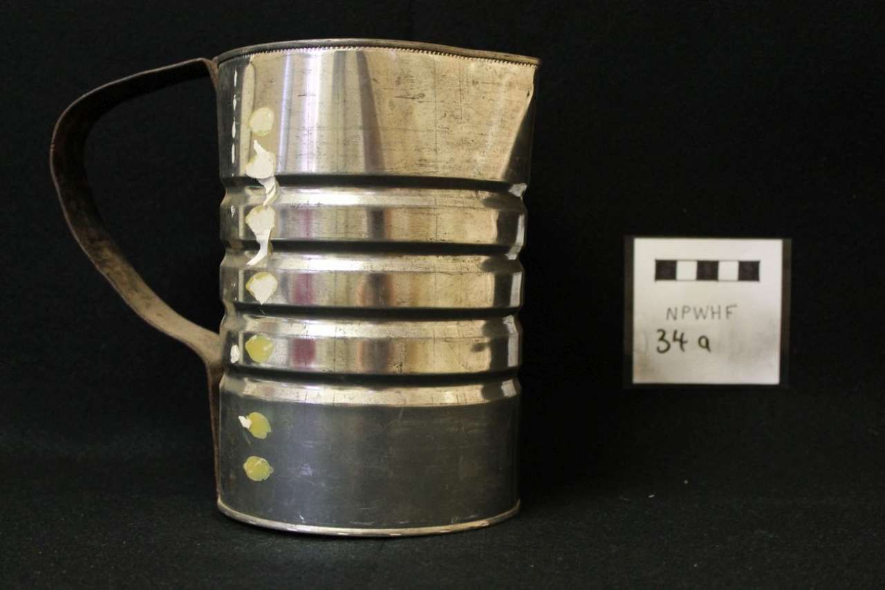 Metal measuring cup with black handle and label card beside it on a dark background
