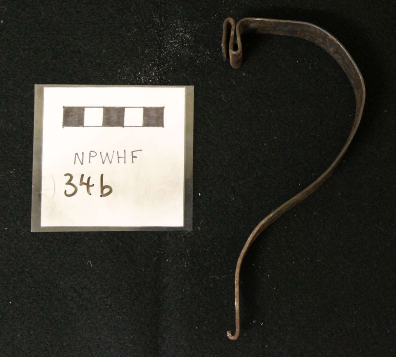 Metal curved hook and small labeled square card on a black background