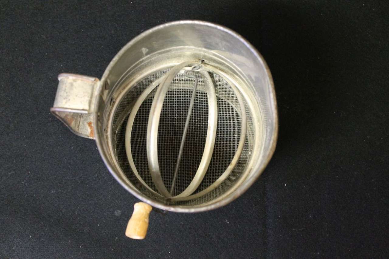 Metal mesh tea infuser cup with handle, viewed from above on a black background