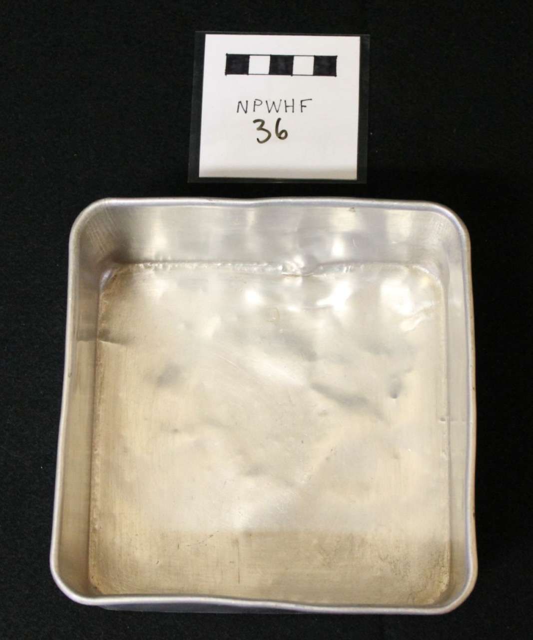 Metal tray with a small labeled card above it on a black background