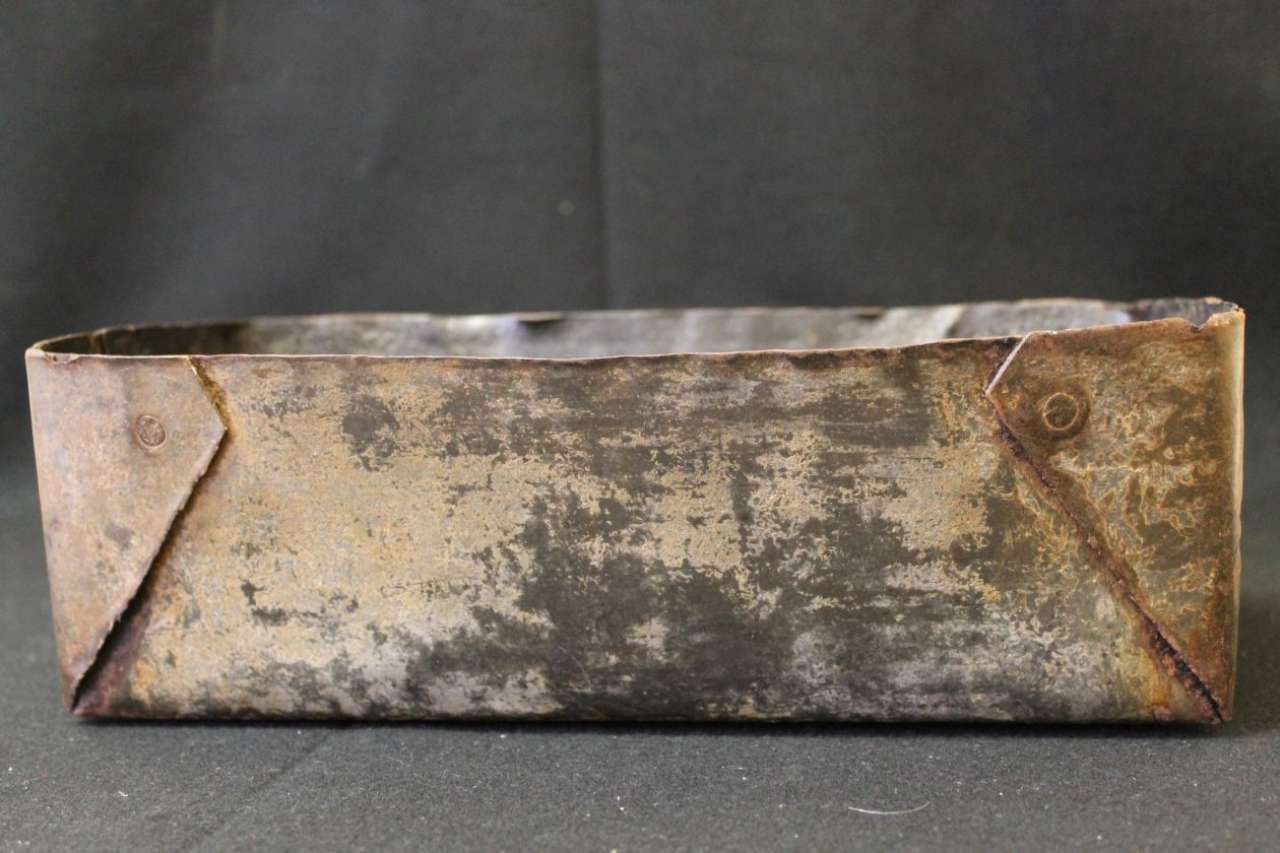 Rusty rectangular metal box with folded corners on a dark background