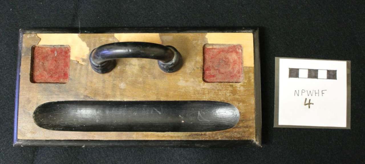 Black handle and long black bar in a tan box, with a small labeled card beside it.