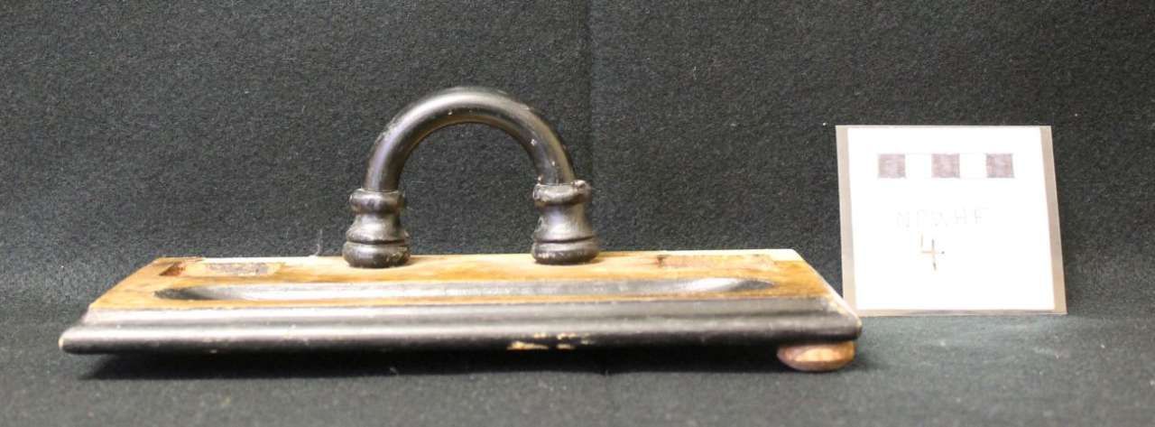 Metal handbell on a wooden base beside a small white display card on a gray background