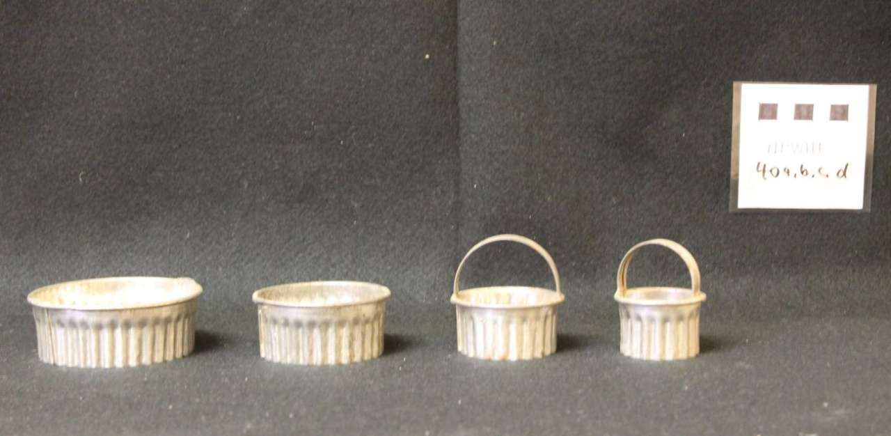 Four white ribbed containers with handles on a dark surface, plus a small wall switch in the background