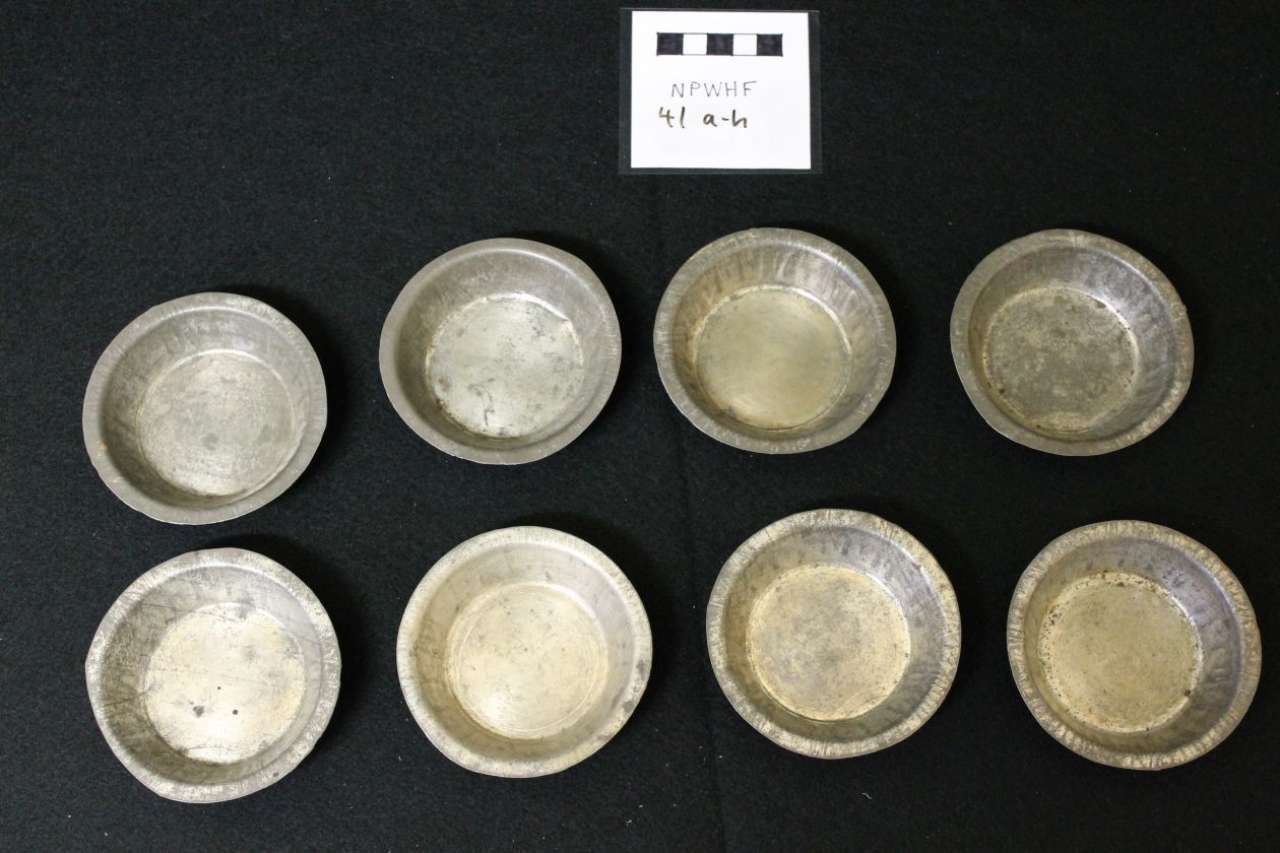 Eight small metal bowls arranged in two rows on a black background with a small label above them