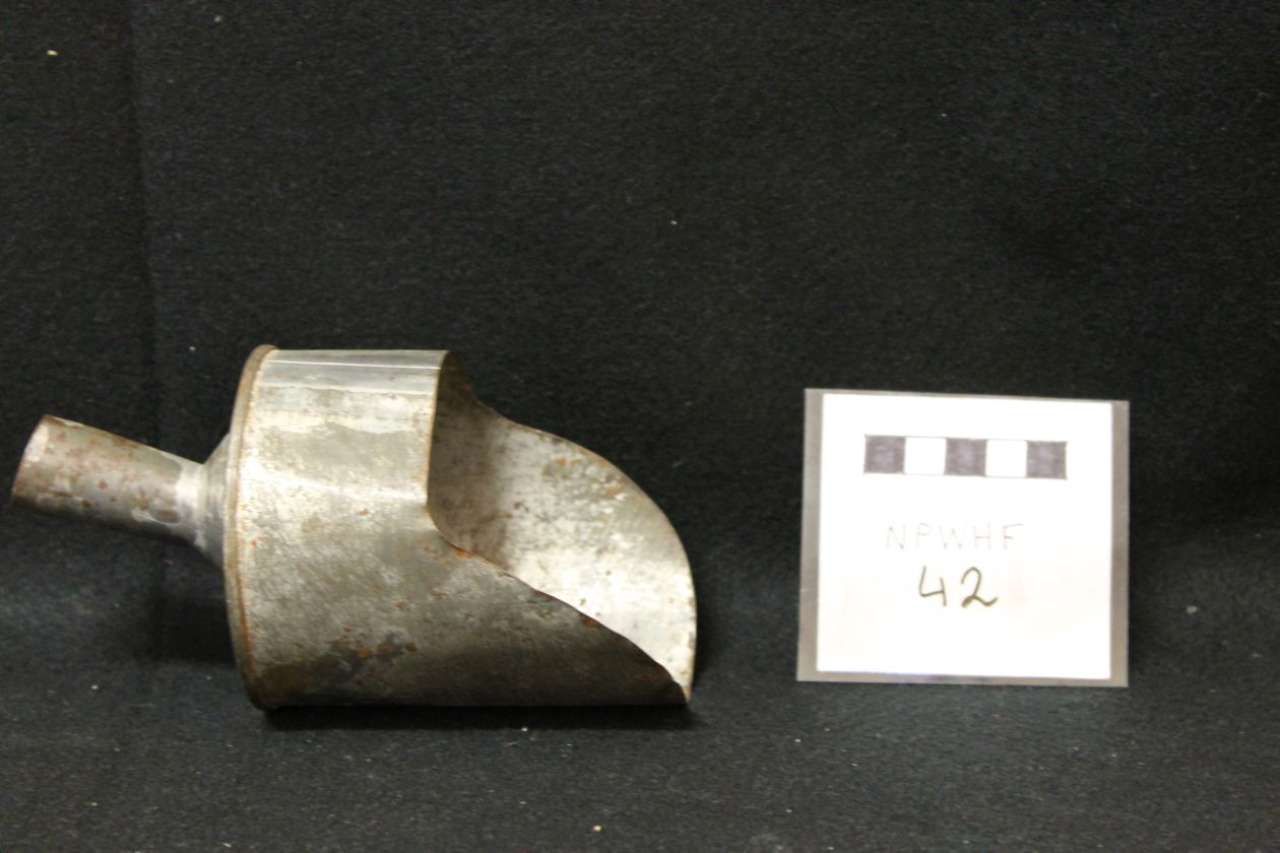 Small metal scoop with a short handle beside a labeled card marked “42” on a black background