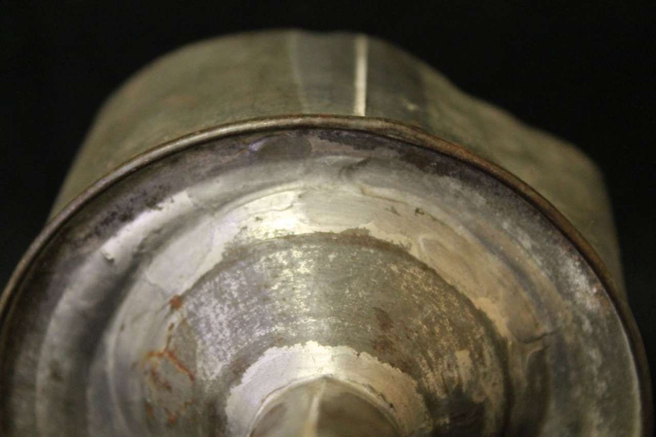 Close-up of a metal cylindrical object with a worn, reflective surface and dark background