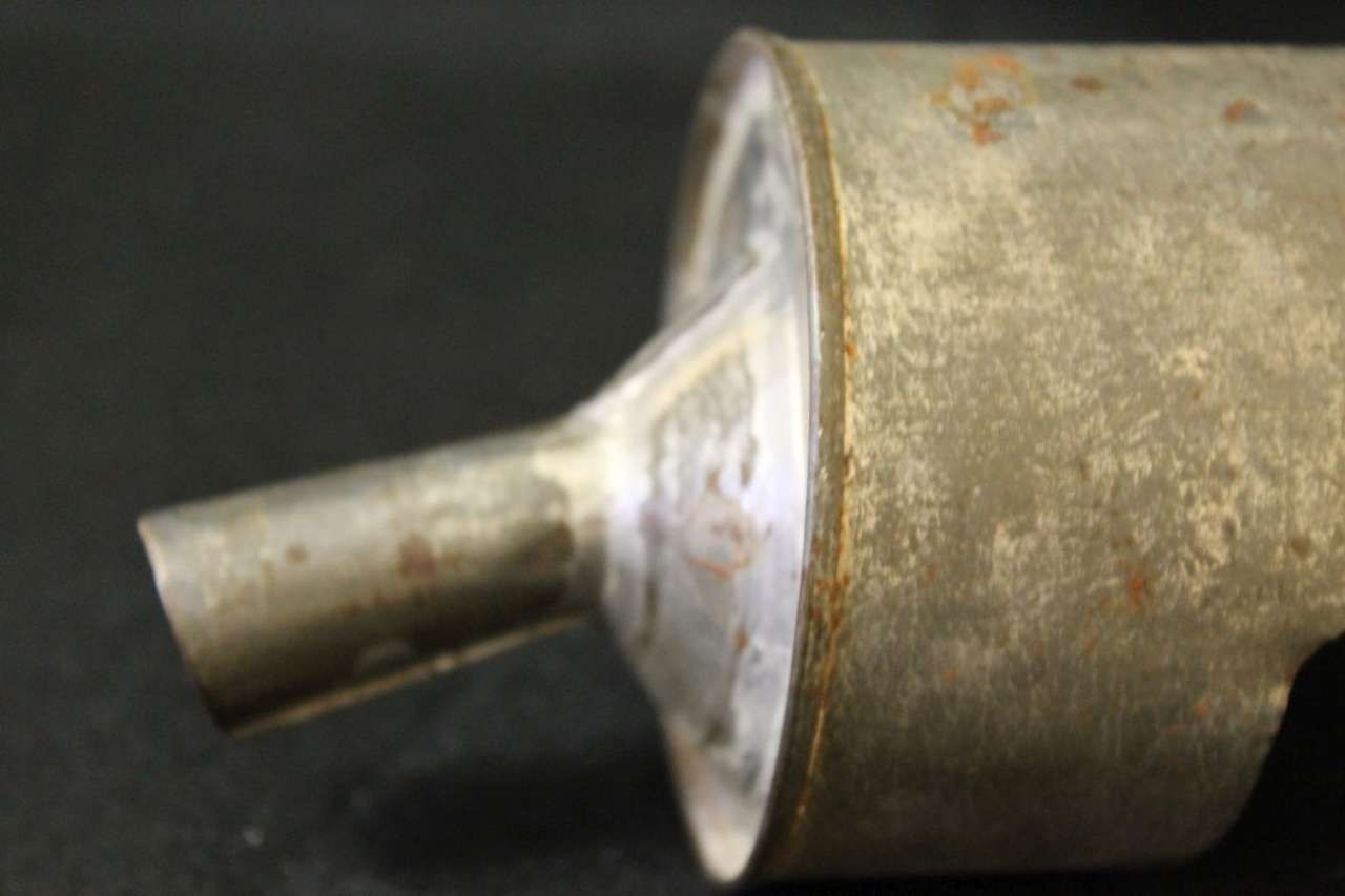 Close-up of a rusty metal pipe or nozzle attached to a cylindrical fitting on a dark background