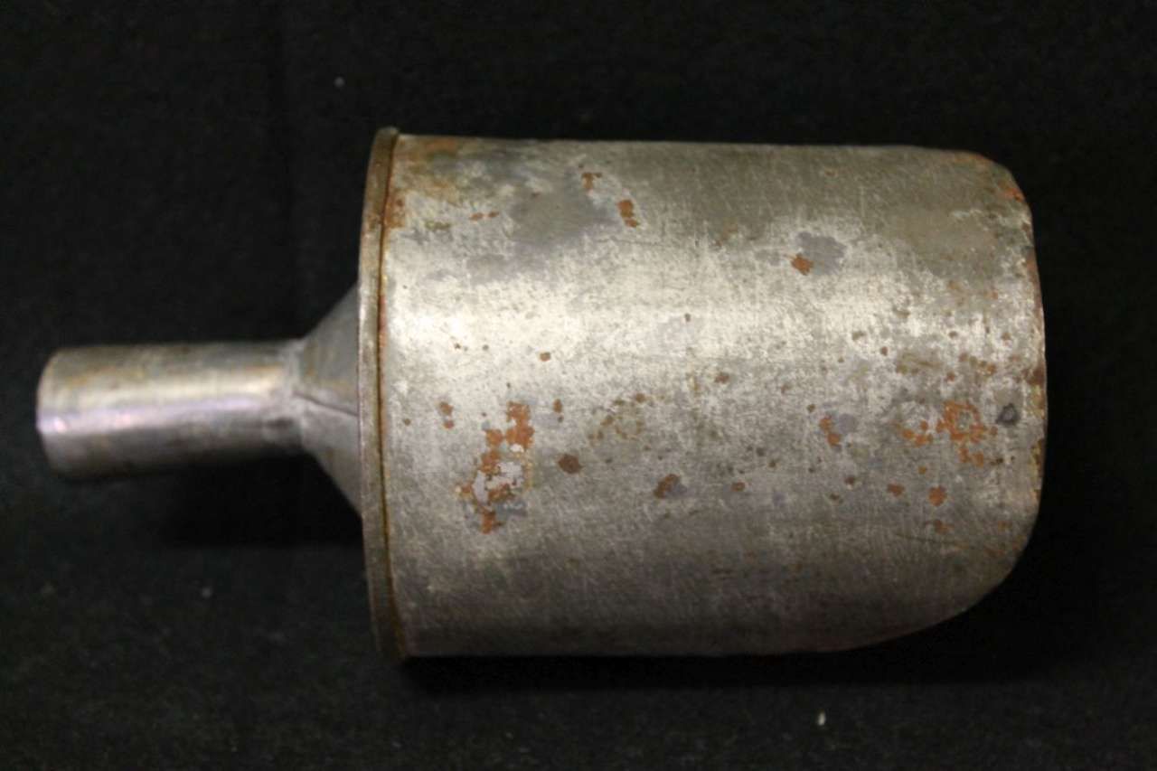 A small rusty metal cylindrical object with a short protruding nozzle on a dark background