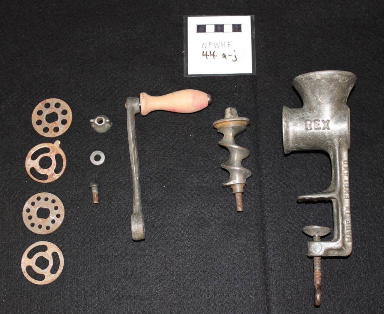 Assorted metal hand tools and parts arranged on a black background, including a crank, gears, and a vise-like tool.