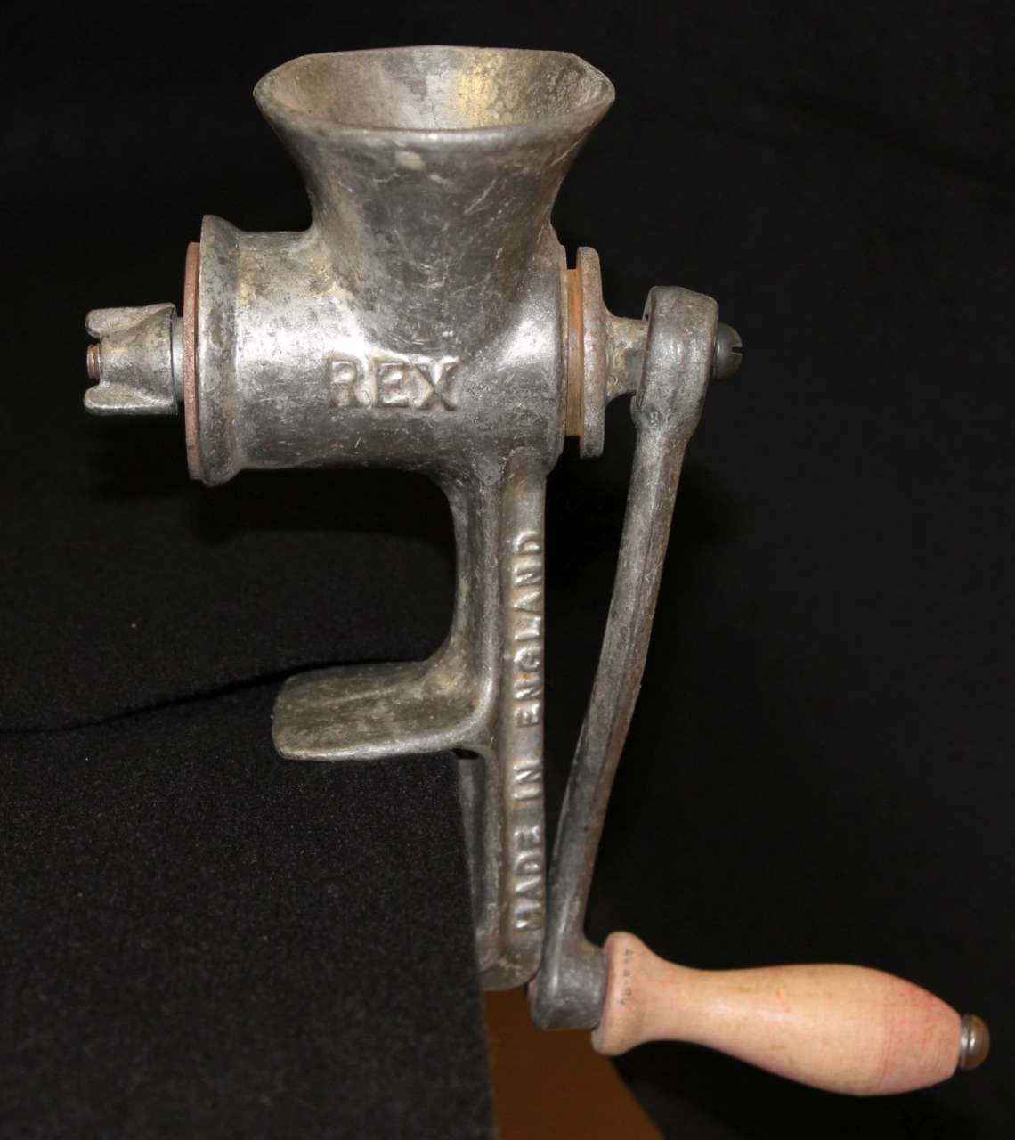 Vintage hand-crank metal meat grinder with wooden handle on a black background