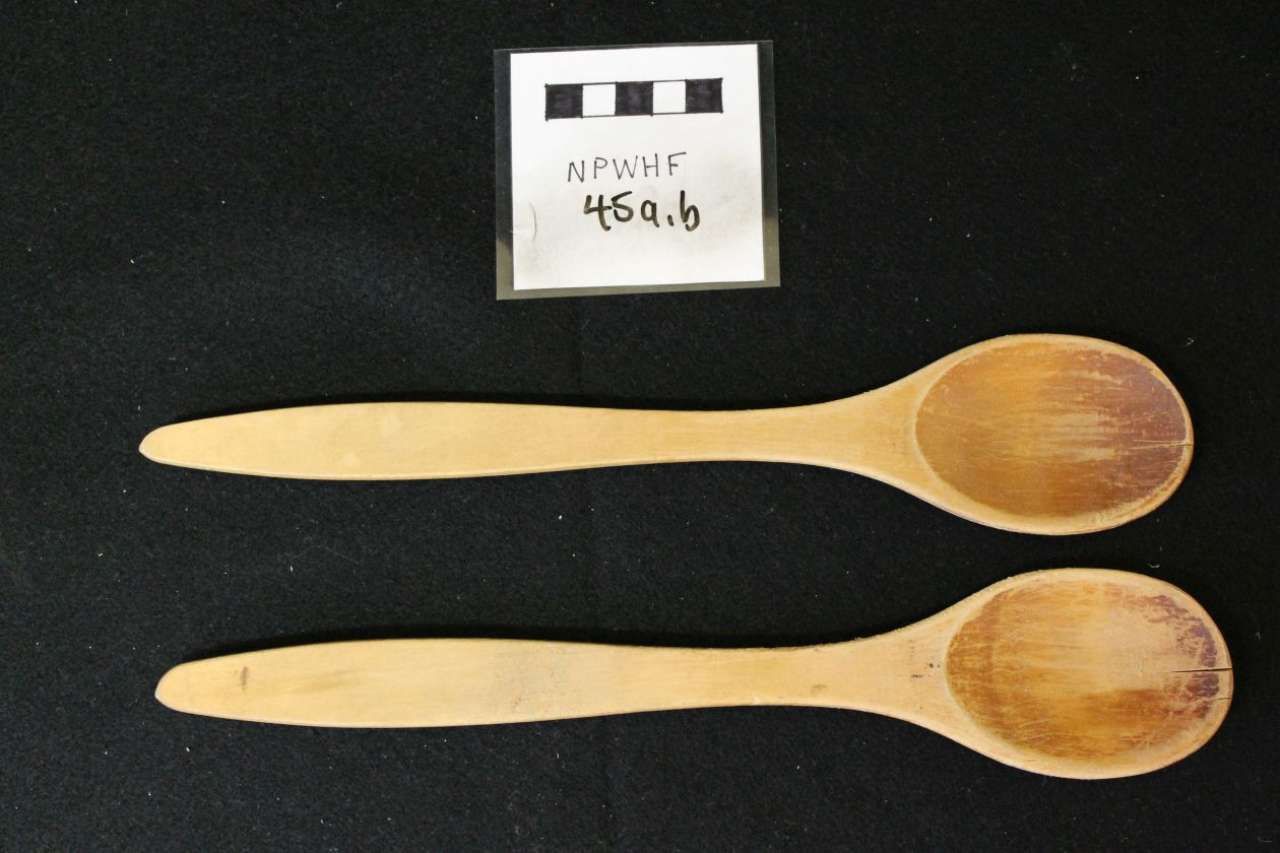 Two wooden spoons on a black background beside a small labeled card.