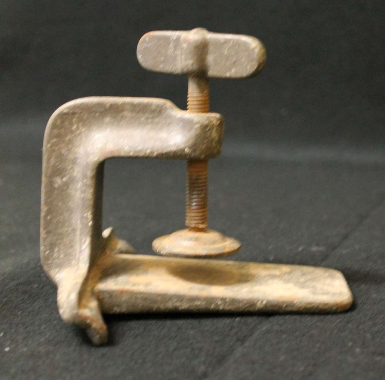 Small metal C-clamp with a threaded screw on a dark background