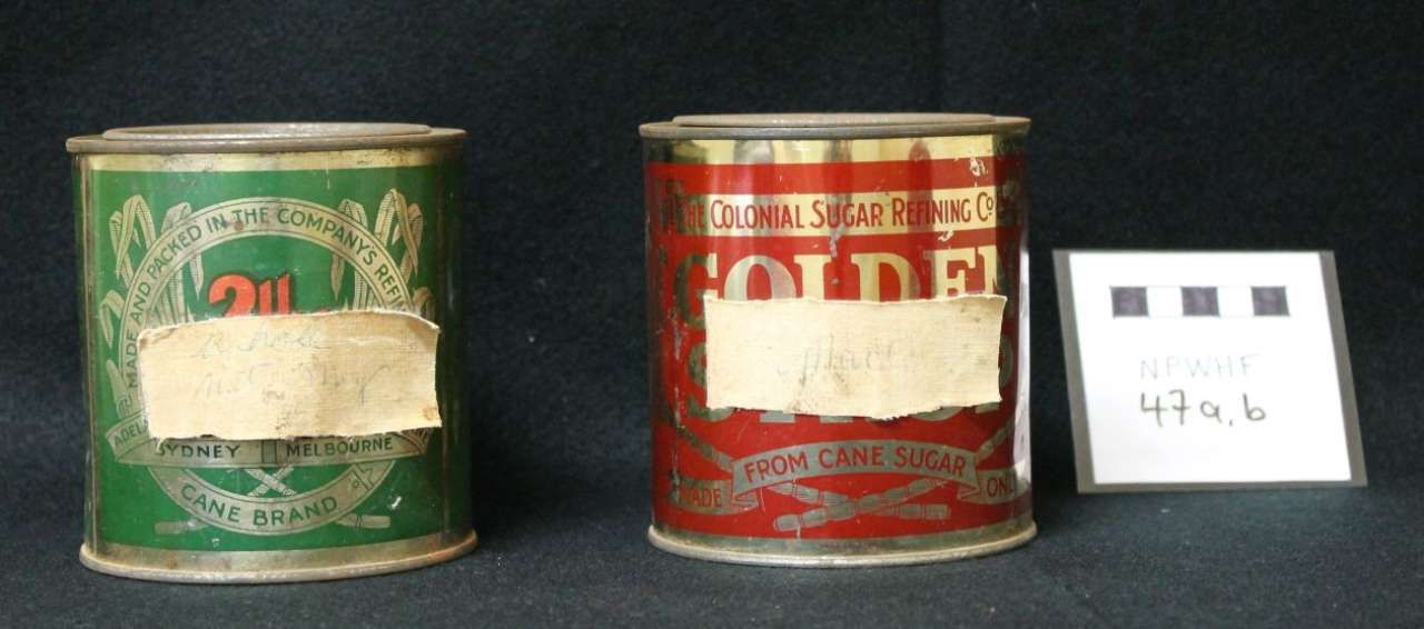 Two vintage painted tin cans, green and red, beside a small white label card.