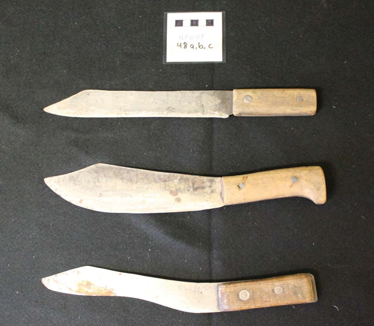 Three rusty metal knives with worn handles displayed on a black background