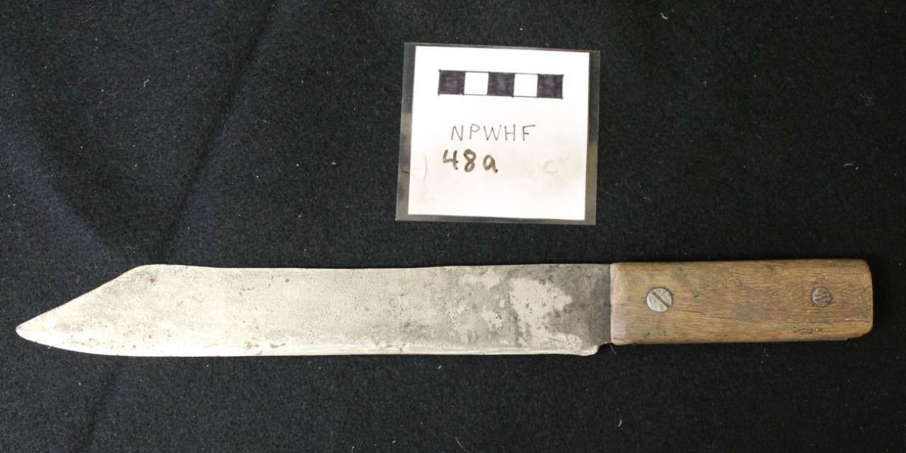 Rusty metal knife with wooden handle beside a small handwritten label on a black background