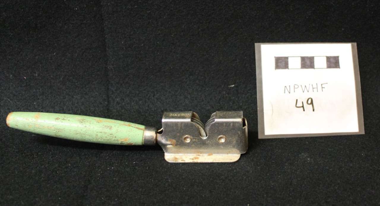 Green-handled metal tool beside a small numbered label on a black background.