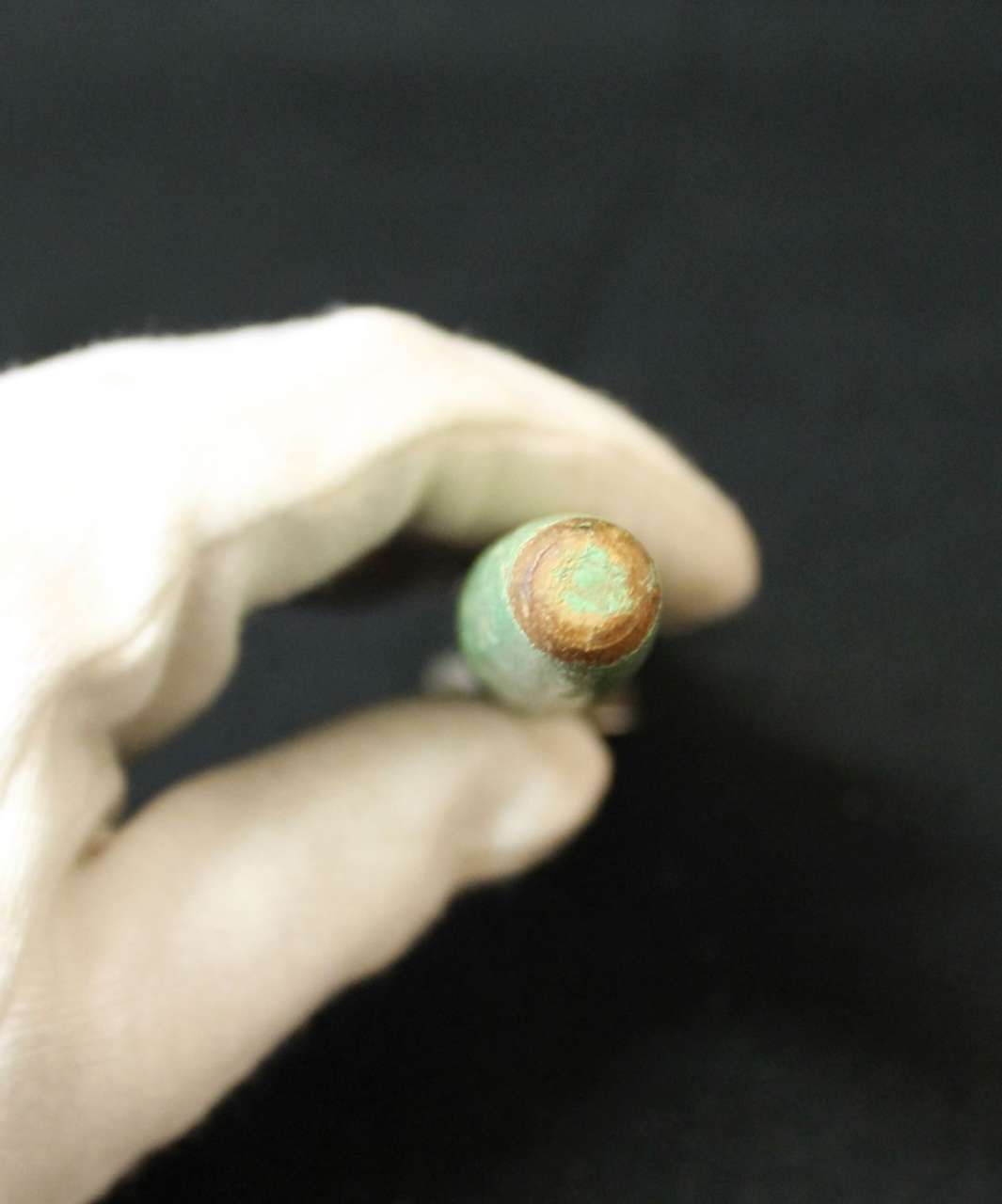 Hand holding a small green object with a rusty orange end against a dark background