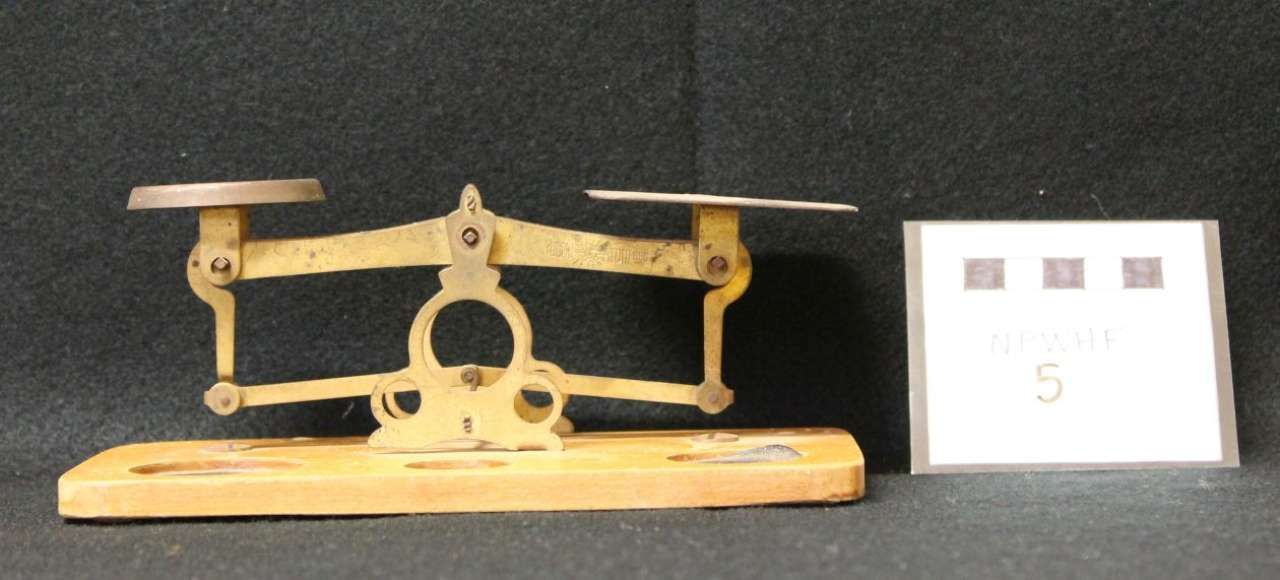 Antique brass mechanical device on a wooden base beside a small white display card