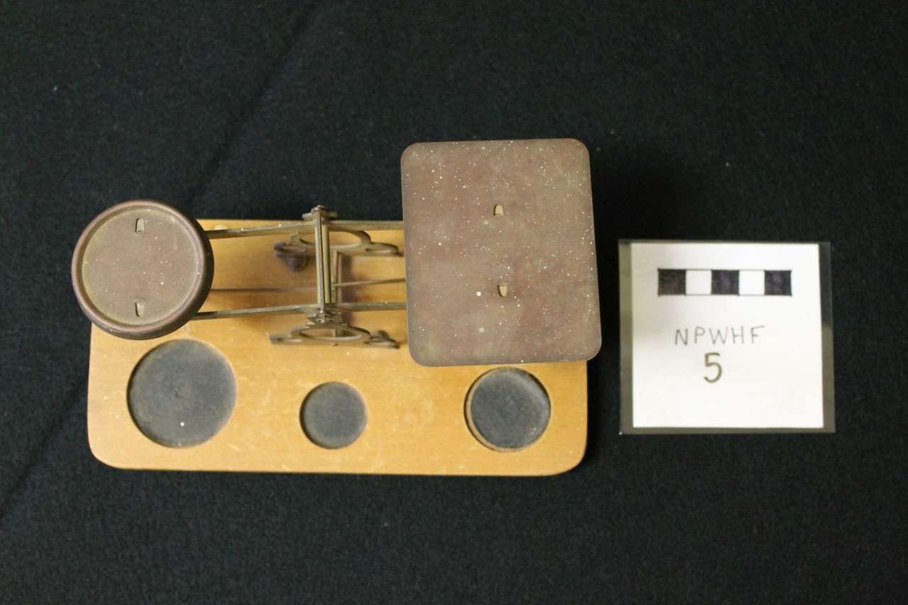 Small wooden mouse trap beside a white evidence marker labeled 5 on a dark surface