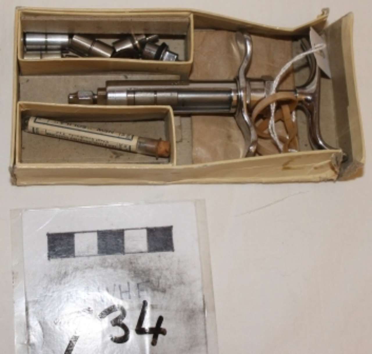 Open cardboard box with metal tools and parts beside a small black-and-white labeled card.