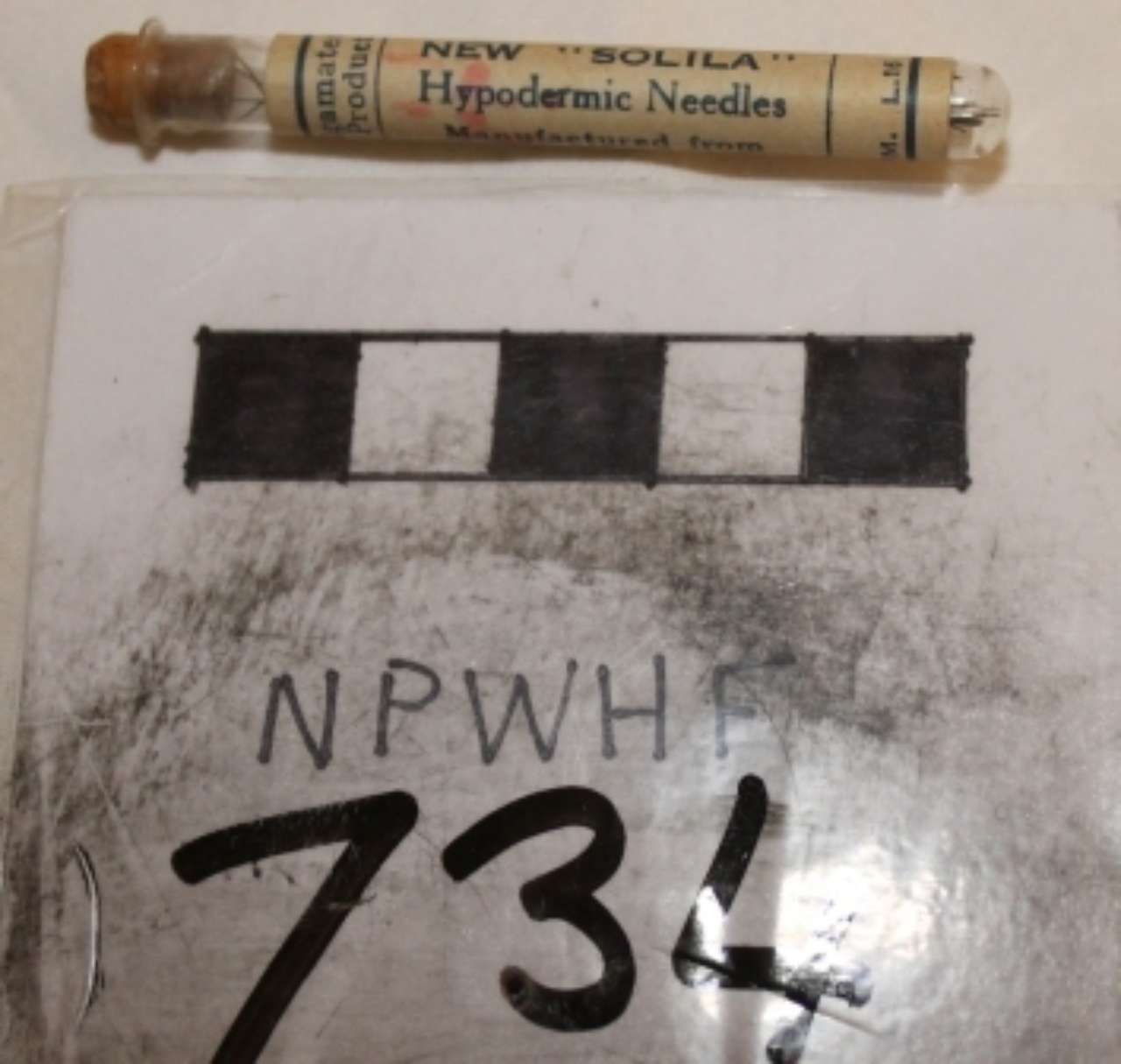Hypodermic needle in a small tube above a black-and-white evidence marker labeled NPWH 734