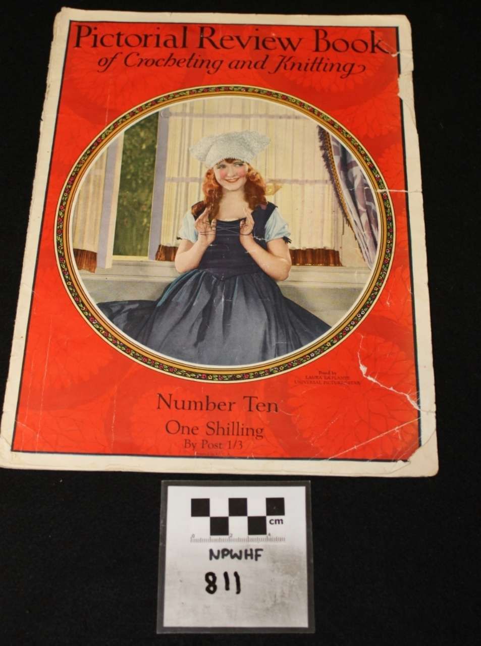 Red cover of a Pictorial Review Book featuring a woman in a blue dress by a window, with a label below.