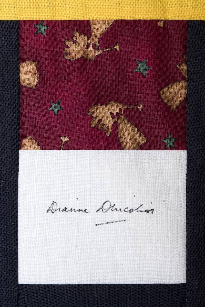Maroon leaf-patterned fabric with a white label signed “Dianne Lincoln”