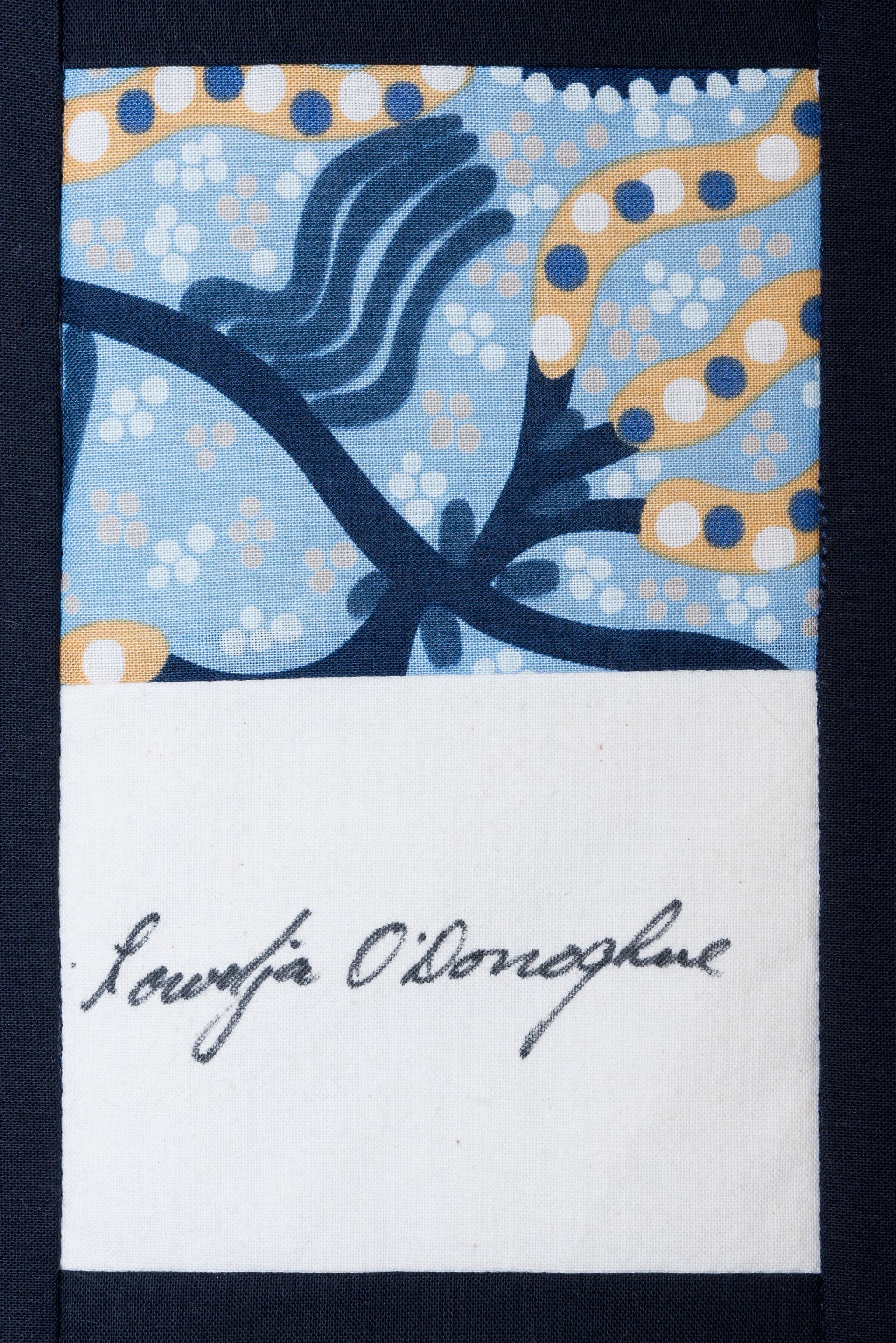 Blue patterned fabric label with cursive signature on white background