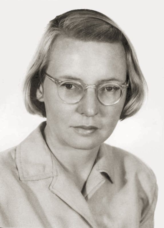 Portrait of a person with glasses and short hair, wearing a light jacket, against a plain background